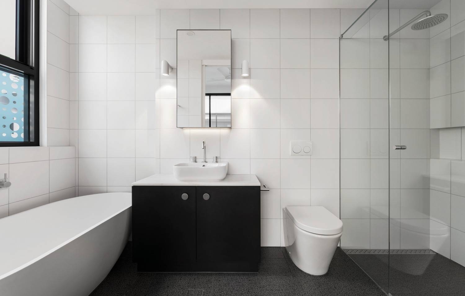 Moderni mustavalkoinen kylpyhuone. Oikealla sadesuihku ja lasiseinä, vasemmalla valkoinen kylpyamme.