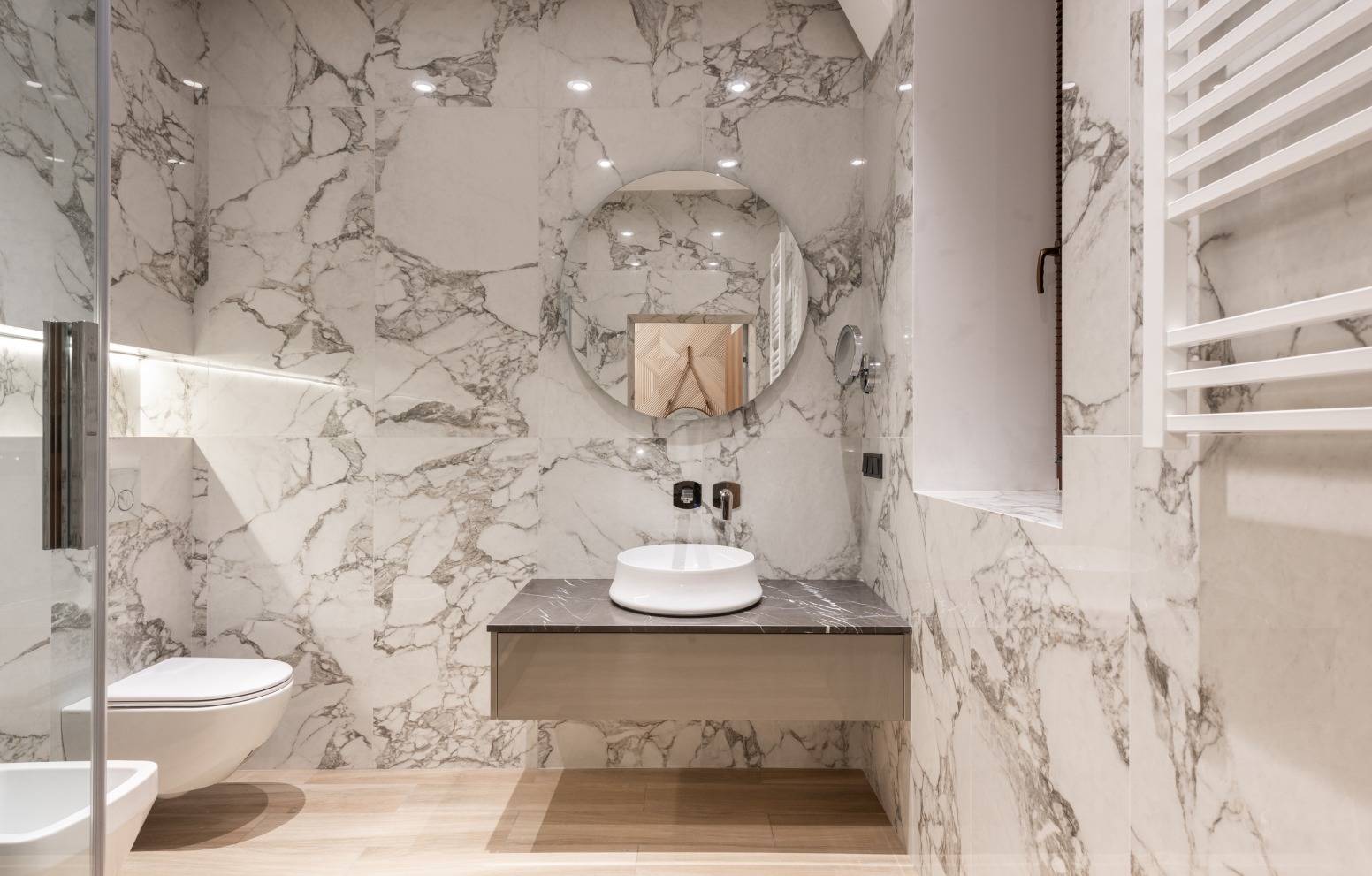 Kaunis wc, jossa peili, lavuaari sekä paljon marmoripintoja.